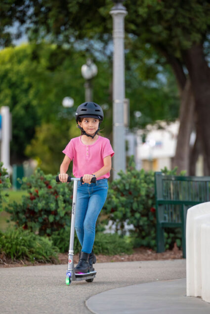 A girl riding a Color Rave Electric Scooter at a park